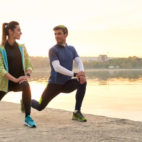 Young running couple warming up and stretching before running outdoors in the morning